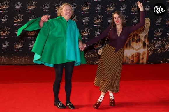 Sur la photo, Philippe Katerine porte une spectaculaire tenue composée de larges pans de tissu vert vif et turquoise, qui forment une silhouette ample et sculpturale autour de son corps. 

Philippe Katerine et sa fille Edie Blanchard - Photocall de la 28ème édition des NRJ Music Awards 2026 au palais des festivals et des congrès de Cannes, le 23 octobre 2026.  © Dominique Jacovides / Bestimage