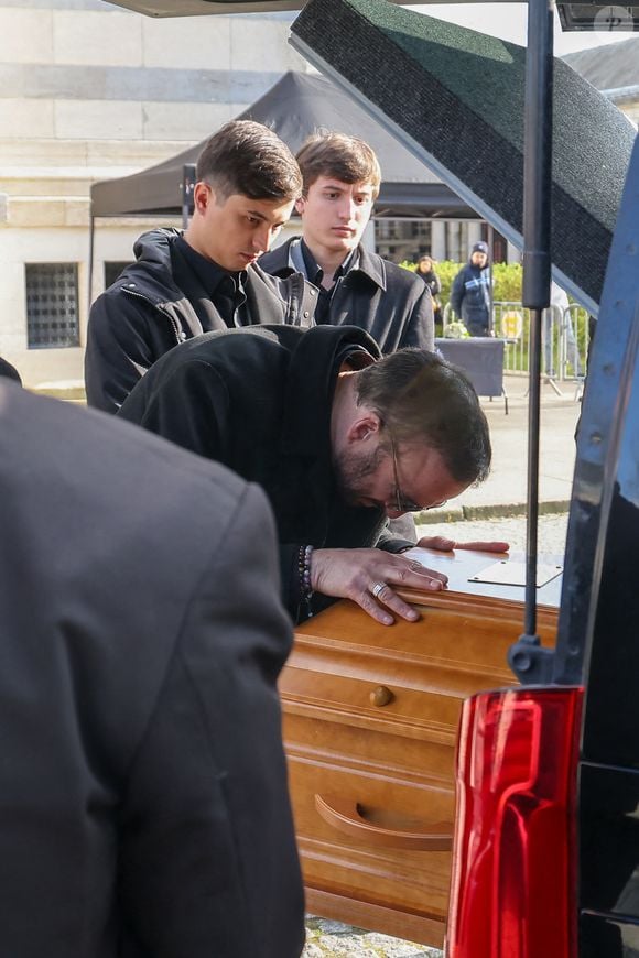 Le veuf Michel Ferracci embrasse le cercueil de la défunte, sous le regard de ses fils Enzo et Maël à la sortie des obsèques d'Emilie Dequenne au cimetière Père Lachaise à Paris, France, le 26 mars 2025. © Cyril Moreau/Bestimage
