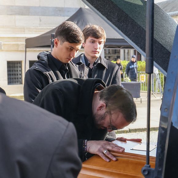 Le veuf Michel Ferracci embrasse le cercueil de la défunte, sous le regard de ses fils Enzo et Maël à la sortie des obsèques d'Emilie Dequenne au cimetière Père Lachaise à Paris, France, le 26 mars 2025. © Cyril Moreau/Bestimage