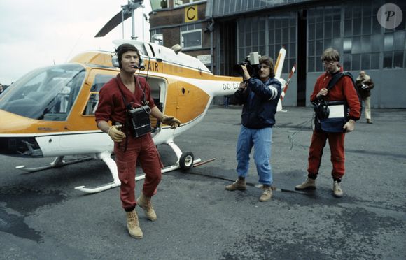 Archives - En France, Philippe DE DIEULEVEULT, devant l'hélicoptère, vêtu de sa combinaison rouge, portant son casque d'écoute et son poste émetteur, le cameraman, Patrick FABRY et le responsable du magnétoscope, Serge BEAUPERE lors de l'émission La chasse aux trésors en mai 1983