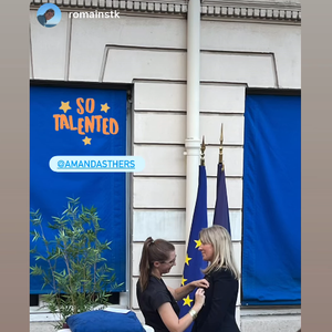On y découvre l'instant solennel où la précieuse médaille, d'abord reposée sur un élégant coussin bleu, lui est épinglée sur le revers de sa veste.

Amanda Sthers décorée pour son parcours.