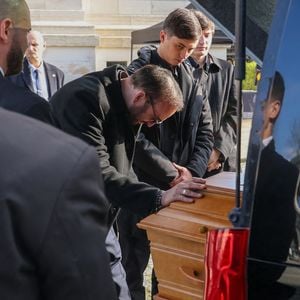 Le veuf Michel Ferracci embrasse le cercueil de la défunte, sous le regard de ses fils Enzo et Maël à la sortie des obsèques d'Emilie Dequenne au cimetière Père Lachaise à Paris, France, le 26 mars 2025. © Cyril Moreau/Bestimage