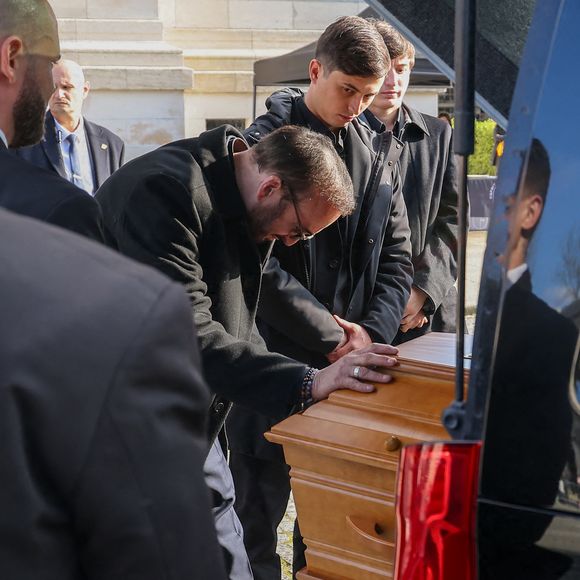 Le veuf Michel Ferracci embrasse le cercueil de la défunte, sous le regard de ses fils Enzo et Maël à la sortie des obsèques d'Emilie Dequenne au cimetière Père Lachaise à Paris, France, le 26 mars 2025. © Cyril Moreau/Bestimage