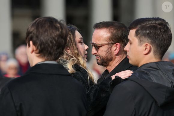 Michel Ferracci serre dans ses bras sa belle-fille, Milla Savarese, la fille de la défunte, sous le regard de ses fils Maël et Enzo Ferracci à la sortie des obsèques d'Emilie Dequenne au cimetière Père Lachaise à Paris, France, le 26 mars 2025. © Cyril Moreau/Bestimage