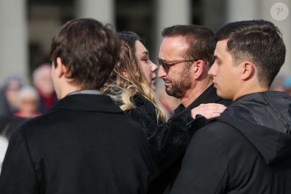 Michel Ferracci serre dans ses bras sa belle-fille, Milla Savarese, la fille de la défunte, sous le regard de ses fils Maël et Enzo Ferracci à la sortie des obsèques d'Emilie Dequenne au cimetière Père Lachaise à Paris, France, le 26 mars 2025. © Cyril Moreau/Bestimage