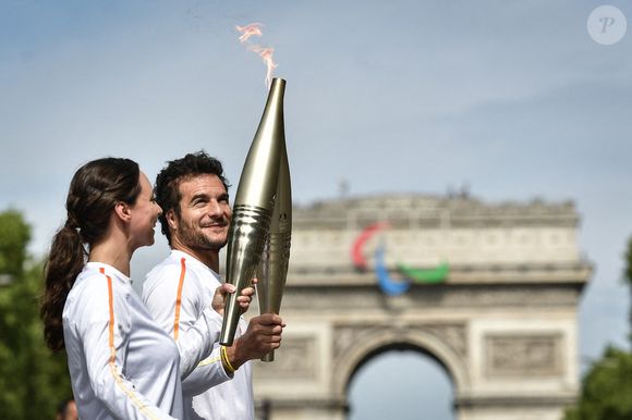 Le chanteur franco-israélien Amir Haddad transmet la flamme olympique à la pâtissière française Nina Metayer sur les Champs-Elysées devant l'Arc de Triomphe lors du relais de la flamme olympique à Paris le 15 juillet 2024. Photo by Firas Abdullah/ABACAPRESS.COM