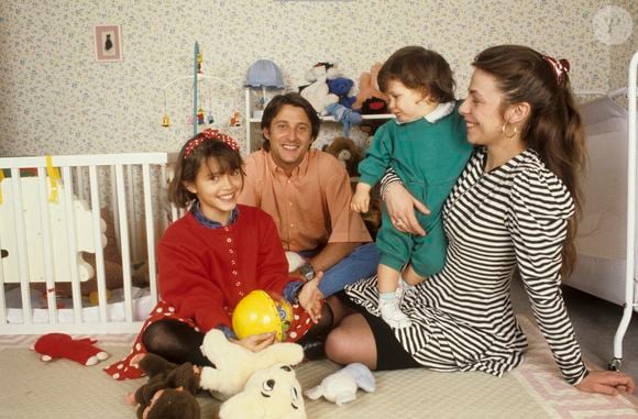 Archives - En France, à Neuilly-Sur-Seine, dans une chambre d'enfant, portrait de Antoine de Caunes assis par terre, avec sa compagne Agnès Leglise tenant leur fils Louis de Caunes, et sa fille Emma de Caunes coiffée d'un serre-tête et tenant un jouet. Date inconnue
© Michel Ristroph via Bestimage