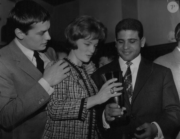 08 août 1961 - Romy Schneider remet un trophée de boxe à un poids léger tunisien : Romy Schneider et Alain Delon, l’un des couples les plus célèbres du cinéma français, ont remis aujourd’hui un trophée de boxe au poids léger tunisien Omrane Sadok lors d’un cocktail. La photo montre Romy Schneider remettant la coupe à Omrane Sadok. Alain Delon, son partenaire et fiancé, la tient affectueusement par l’épaule. (Selon les rumeurs, Delon serait le partenaire de B.B. dans son prochain film.) (Crédit image : © Keystone Press Agency/ZUMA Press Wire)
