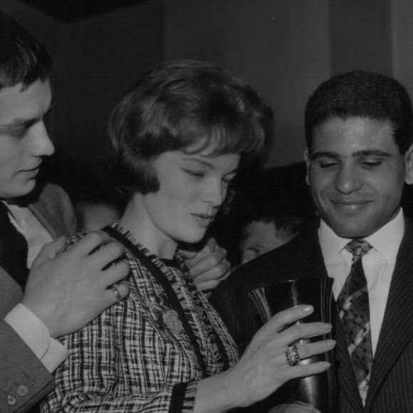 08 août 1961 - Romy Schneider remet un trophée de boxe à un poids léger tunisien : Romy Schneider et Alain Delon, l’un des couples les plus célèbres du cinéma français, ont remis aujourd’hui un trophée de boxe au poids léger tunisien Omrane Sadok lors d’un cocktail. La photo montre Romy Schneider remettant la coupe à Omrane Sadok. Alain Delon, son partenaire et fiancé, la tient affectueusement par l’épaule. (Selon les rumeurs, Delon serait le partenaire de B.B. dans son prochain film.) (Crédit image : © Keystone Press Agency/ZUMA Press Wire)