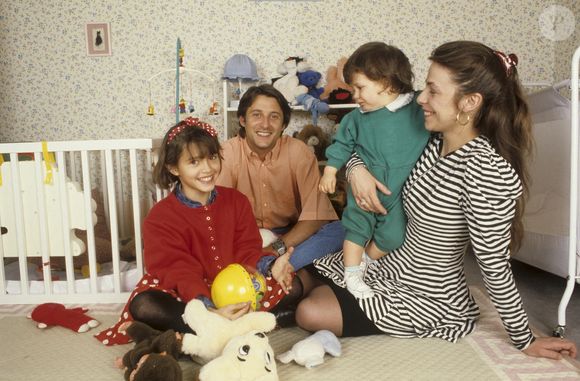 Archives - En France, à Neuilly-Sur-Seine, dans une chambre d'enfant, portrait de Antoine de Caunes assis par terre, avec sa compagne Agnès Leglise tenant leur fils Louis de Caunes, et sa fille Emma de Caunes coiffée d'un serre-tête et tenant un jouet. Date inconnue
© Michel Ristroph via Bestimage
