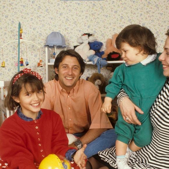 Archives - En France, à Neuilly-Sur-Seine, dans une chambre d'enfant, portrait de Antoine de Caunes assis par terre, avec sa compagne Agnès Leglise tenant leur fils Louis de Caunes, et sa fille Emma de Caunes coiffée d'un serre-tête et tenant un jouet. Date inconnue
© Michel Ristroph via Bestimage