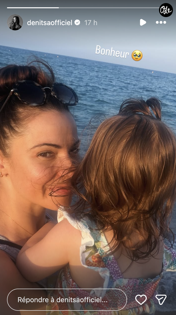 Sur cette image, on découvre Denitsa Ikonomova profitant de l'air marin. Le visage balayé par le vent, des lunettes de soleil à monture écaille remontées sur la tête, elle affiche un sourire naturel et apaisé tout en tenant son enfant serré dans ses bras face à l'étendue bleue.

Denitsa Ikonomova avec sa fille