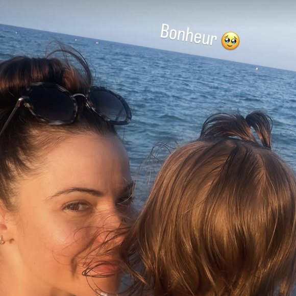 Sur cette image, on découvre Denitsa Ikonomova profitant de l'air marin. Le visage balayé par le vent, des lunettes de soleil à monture écaille remontées sur la tête, elle affiche un sourire naturel et apaisé tout en tenant son enfant serré dans ses bras face à l'étendue bleue.

Denitsa Ikonomova avec sa fille