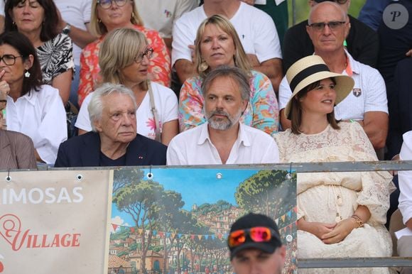 Semi-exclusif - Michel Sardou, Romain Sardou et sa compagne Kym Thiriot enceinte - Michel Sardou rend hommage à son père en famille lors du premier trophée de pétanque "Fernand Sardou" à Bormes-les-Mimosas le 29 mai 2026. Le célèbre chanteur est venu en famille avec sa femme, son fils Romain avec son fils de deux ans et demi et de sa compagne enceinte de son deuxième enfant.
La première édition du Trophée Fernand Sardou est organisée du 29 au 31 mai au coeur du village de Bormes les Mimosas. Une initiative portée par Michel et son fils Romain, pour rendre hommage à leur illustre parent Fernand Sardou au travers d'un tournoi de pétanque.
En lien avec la municipalité et l'Amicale Bouliste Borméenne (ABB), un premier Trophée Fernand Sardou sera organisé avec deux grands temps forts : Le vendredi, dès 18h, un tournoi d'exhibition sera proposé et verra s'affronter 16 triplettes. Puis un concours fédéral à pétanque sera organisé le weekend et ouvert à tous les amateurs. 128 équipes seront réparties sur les sites les plus emblématiques du village, à savoir au boulodrome de la place Saint-François, mais aussi au parc Cigalou, sur le site du château et à l'ancien stade. © Franz Chavaroche/Bestimage