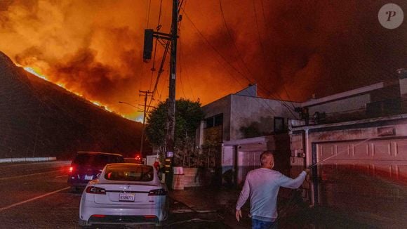 7 janvier 2025, Malibu, Californie, États-Unis : un homme asperge d'eau pour protéger sa maison sur la plage de l'océan Pacifique, à côté de lignes électriques, alors que des nuages de fumée rouge et jaune s'élèvent à l'arrière-plan : Un incendie s'est déclaré le 7 janvier 2025, vu de la PCH (Pacific Coast Highway) dans la ville cossue de Pacific Palisades, à la limite de Malibu, en Californie, en raison des vents exceptionnellement forts de Santa Ana qui ont dépassé les 100 MPH (Image de crédit : © Amy Katz/ZUMA Press Wire).