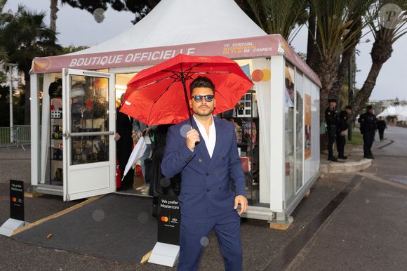 Kev Adams brave la pluie avec un parapluie rouge lors de la première journée du 77ème Festival de Cannes au Palais des Festivals à Cannes, France, le 14 mai 2024 dans le cadre du Photo by Cyril CHATEAU/ABACAPRESS.COM