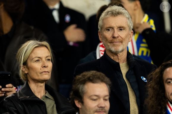 Mais c'est à quelques kilomètres de Paris qu'il vit avec sa famille.

Denis Brogniart et sa femme Hortense - Célébrités dans les tribunes du match de qualification de la Coupe du monde 2026 entre la France contre l'Ukraine (4-0) au Parc des Princes à Paris le 13 novembre 2025. © Cyril Moreau/Bestimage