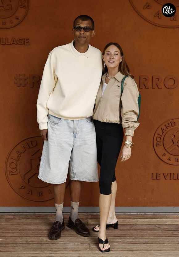 Décontracté avec ses lunettes de soleil, un pull blanc, un long short en jean bleu et des mocassins laissant apparaître ses grandes chaussettes, Stromae a pris la pose avec son épouse...

Stromae et sa femme Coralie Barbier lors des Internationaux de France de Tennis de Roland Garros 2026, à Paris, France, le 7 juin 2026. © Jacovides-Moreau/Bestimage