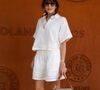 Elle a accessoirisé sa tenue estivale avec un sac en raphia, de larges lunettes et un foulard aux motifs de raquettes couleur ocre, à nouveau de la marque au crocodile.

Nolwenn Leroy au village lors des Internationaux de France de Tennis de Roland Garros 2026. Paris, le 28 mai 2026.

© Jacovides / Moreau / Bestimage