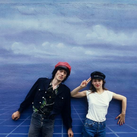En France, durant leur tournée, Catherine Ringer et Fred Chichin, portant une casquette, debout devant un fond bleu ciel. © Michel Croizard via Bestimage