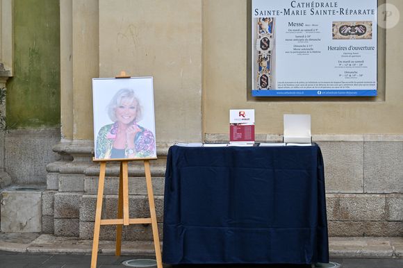 Portrait de la défunte et registre de condoléances à la sortie des obsèques d'Evelyne Leclercq en la cathédrale Sainte-Réparate de Nice, France, le 13 janvier 2026. Une tenue blanche ou claire est souhaitée pour la cérémonie. Ni fleurs, ni couronnes. Selon la volonté de la défunte Evelyne, des dons en faveur du pôle cancérologie Arnault Tzanck pourront être effectués par chèque à l'ordre de FDD AAT ou via un lien numérique HelloAsso - Campagne de dons, Institut du Cancer de Mougins. © Bruno Bebert/Bestimage