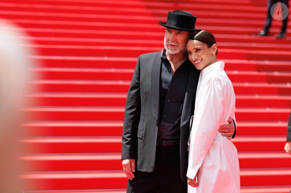 Très affectueux l'un envers l'autre, le couple a pris la pose dans des tenues parfaitement contrastées : un total look noir surmonté d'un chapeau pour l'ancien footballeur, et une robe blanche immaculée pour son épouse.

Eric Cantona et sa femme Rachida Brakni - Montée des marches du film " Soudain " lors du 79ème Festival International du Film de Cannes, le 15 mai 2026. © Jacovides-Moreau / Bestimage